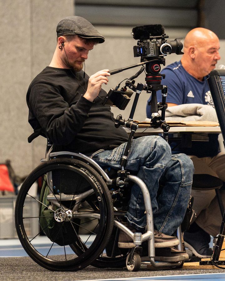 Johannes Springer in der Sporthalle: Er führt vom Rollstuhl aus eine Kamera auf seinem selbst gebauten Haltesystem.