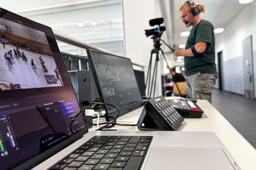 Regieplatz einer Live-Produktion: Laptop mit Spielbild und Scoreboard, zweiter Monitor mit den Kamerabildern, Mischpult — im Hintergrund eine Person an der Kamera.